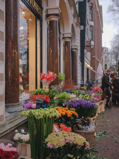 A vibrant display of fresh flowers arranged along the sidewalk outside a florist shop on Bermondsey Street. The assortment includes chrysanthemums, daffodils, and purple lilacs, showcasing a variety o