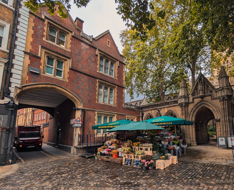 A vibrant flower stall located outdoors beneath a green canopy on Tower Bridge Road, Bermondsey, featuring an extensive array of fresh flowers arranged in wooden crates and buckets. The bouquet arrang